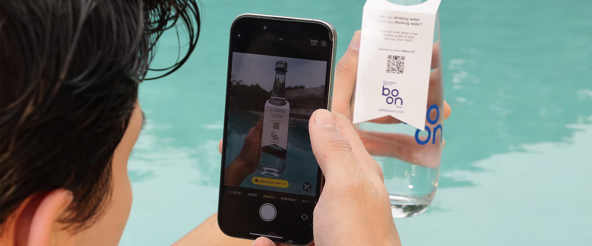 A man photographing a Boon glass water bottle at the poolside