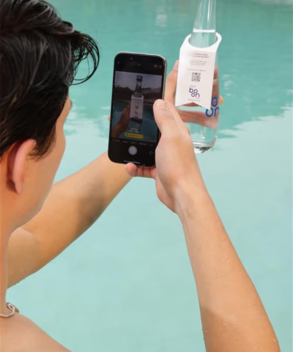 A man photographing a Boon glass water bottle at the poolside