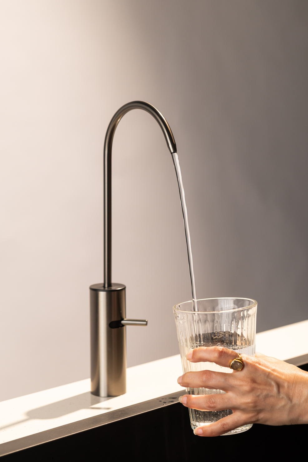 Boon Tap dispensing water into a glass, kitchen counter in soft daylight